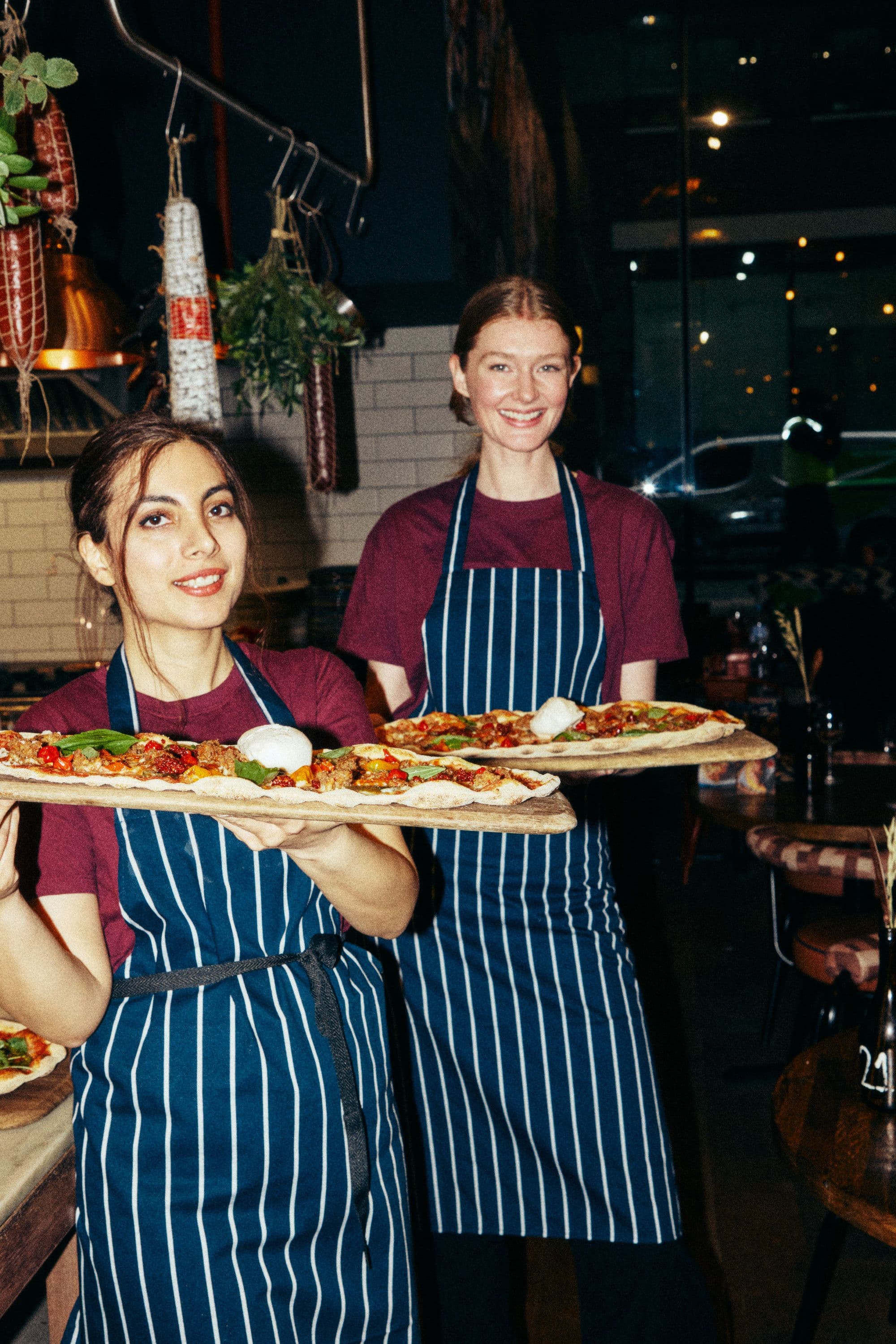 Smiling staff members holding pizzas