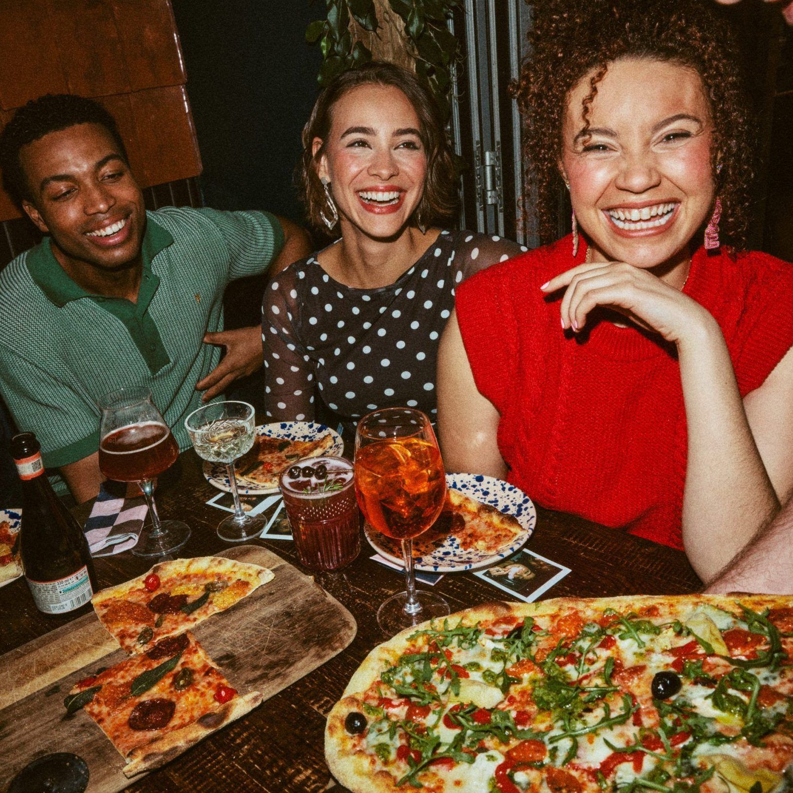 Group of friends smiling at the table with pizza in foreground 
